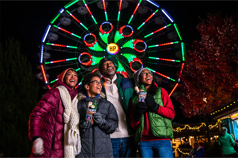 Hersheypark family standing in front of ferris wheel together.