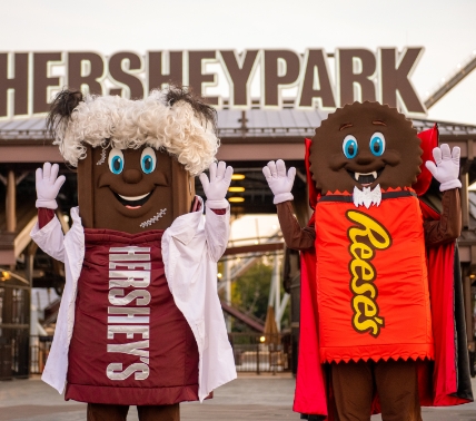 Hershey and Resses posing in Halloween costumes in front of front gate sign.