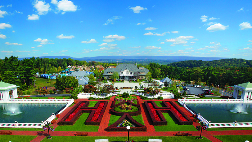 Drone shot of the formal gardens where giant two H's are formed with shrubery, also overlooking two large fountains, a balcony with outdoor seating, and fresh flowers planted around the property.