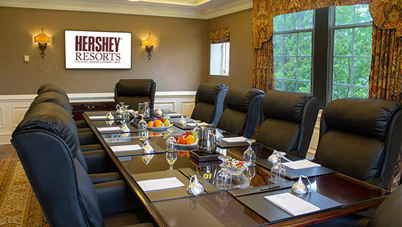 Dimmed meeting room with one large round table with comfortable office chairs lined, the table topped with waters, candies, and notepads at each seat.